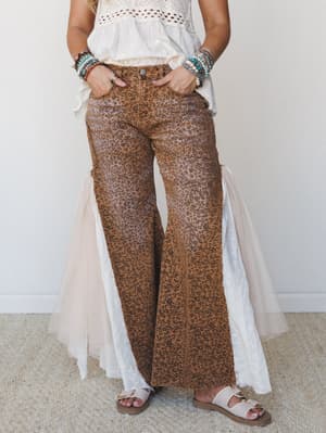 Leopard-print flare pants in a warm camel tone styled with a ruffled cream eyelet top, stacked bead bracelets, and white sandals — the kind of outfit that looks effortless but was definitely thought about.
