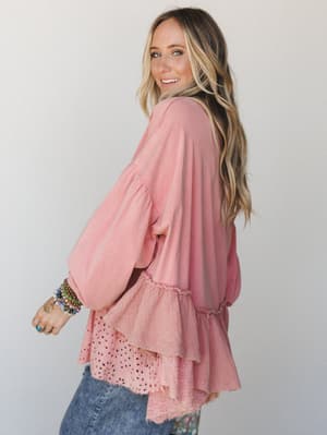 A breezy dusty rose top with mixed-fabric tiered hem detail — the kind of piece that looks intentional with jeans and a stack of bracelets, shot from a three-quarter back angle against a soft studio wall.
