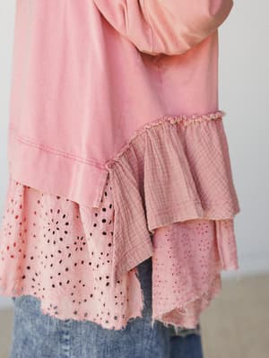 A close-up detail shot of a dusty rose knit top with layered ruffle hem — the mix of eyelet lace, gauze, and raw-edge trim gives it that perfectly undone, handcrafted feel worn over relaxed denim.