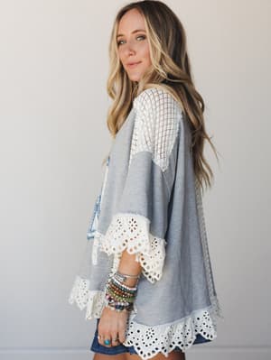 A relaxed grey top with eyelet lace trim at the hem and sleeves and a crochet lace shoulder panel gives this piece an effortlessly boho feel — styled with denim shorts and a wrist full of beaded bracelets, it looks like something you'd reach for on r