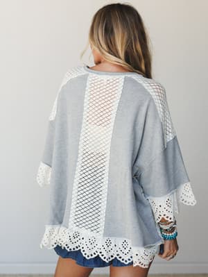 Shot from the back, this relaxed grey top lets its details do the talking — a lattice lace panel down the center, eyelet trim along the hem and sleeves, and that easy oversized silhouette that feels effortless without trying.