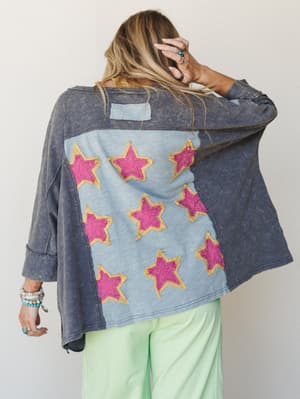 Shot from behind, this oversized acid-wash tee steals the show with a colorblock back panel covered in hot pink star appliqués — styled with mint wide-leg pants and layered boho jewelry for a look that's equal parts vintage and playful.