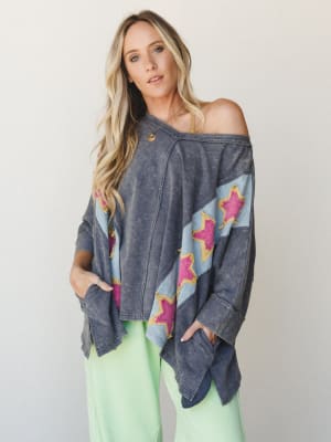 An oversized acid-wash top with bold star appliqués worn off-the-shoulder, paired with mint green pants — the kind of piece that looks like it wandered out of a vintage concert tee collection and decided to stay.