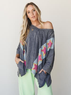An oversized acid-wash top with bold star appliqués worn off-the-shoulder, paired with mint green pants — the kind of piece that looks like it wandered out of a vintage concert tee collection and decided to stay.