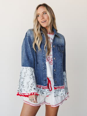 A mixed-media denim jacket with flared bell sleeves in a gray animal print and red pom-pom trim, layered over a white embroidered top and matching shorts — the kind of outfit that shows up to the cookout and quietly steals the show.