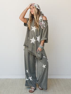 A matching acid-wash star print set — oversized top and wide-leg pants in washed olive — styled with a floral headscarf, stacked bracelets, and sandals for an effortlessly free-spirited look.