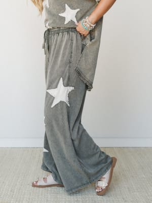 A mineral-washed olive wide-leg pant set with chunky star appliqués, styled with beaded bracelets and white buckle sandals — the kind of outfit that feels like you tried just enough.