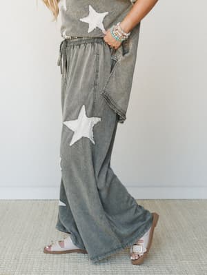A mineral-washed olive wide-leg pant set with chunky star appliqués, styled with beaded bracelets and white buckle sandals — the kind of outfit that feels like you tried just enough.