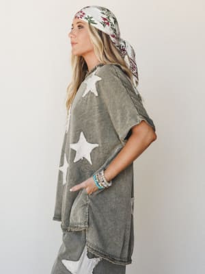 An oversized acid-wash olive set with chenille star appliqués, styled with a floral head scarf and stacked bead bracelets — the kind of outfit that looks effortless but is clearly very intentional.