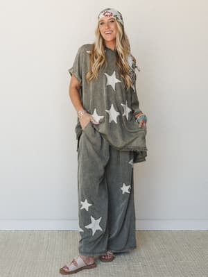 A matching mineral-washed olive star-print set — oversized top and wide-leg pants — styled with a floral headscarf, turquoise beaded bracelet, and slide sandals for an effortlessly free-spirited, lived-in look.