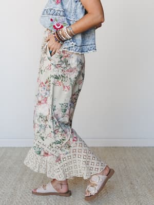 A side-profile shot of a floral maxi pant with a crochet lace hem paired with an embroidered denim crop top and white buckle sandals — the kind of outfit that feels both put-together and completely relaxed.