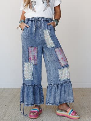 Wide-leg acid wash denim pants with floral and abstract patchwork panels steal the show here — paired with a graphic tee, stacked bracelets, and rainbow platform sandals for a look that's equal parts nostalgic and totally its own thing.