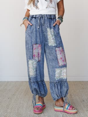 Acid-wash denim balloon pants with mixed floral and plaid patchwork panels, gathered ruffle hems with tie closures, styled with a graphic tee and rainbow platform sandals — the kind of pants that make a whole personality statement without trying.