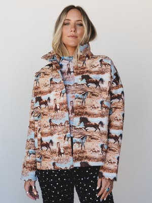 A boxy tapestry jacket covered in a wild horse scenic print is styled with matching separates and sparkly black sequin pants — the kind of outfit that has a whole personality before you even say hello.