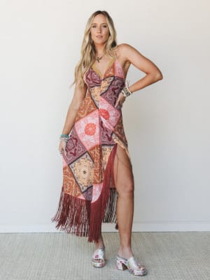 A patchwork bandana-print halter midi dress with deep burgundy fringe trim and a high leg slit, styled with floral platform mules and stacked bracelets — free-spirited and confident, like she's already got a story to tell.