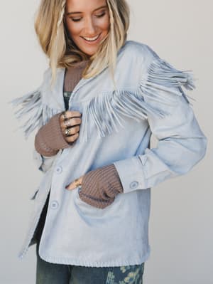 Woman wearing a light blue fringed jacket with brown cuffs against a plain background