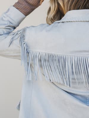 Light blue denim jacket with fringe details on a neutral background