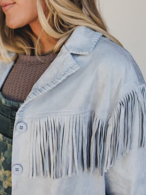 Light blue denim jacket with fringe details worn by a person.