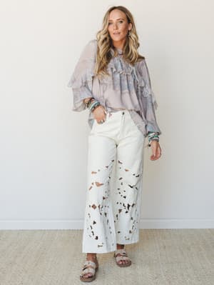 A flowy paisley blouse in dusty lavender-mocha with tiered ruffle detailing is paired with wide-leg white cutwork pants and neutral sandals — the kind of outfit that looks effortless but clearly wasn't an accident.