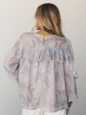 A flowy paisley blouse photographed from the back, showing off its tiered ruffle trim across the shoulders and dramatic ruffle sleeves — the kind of top that moves when you walk and makes even a Tuesday feel intentional.