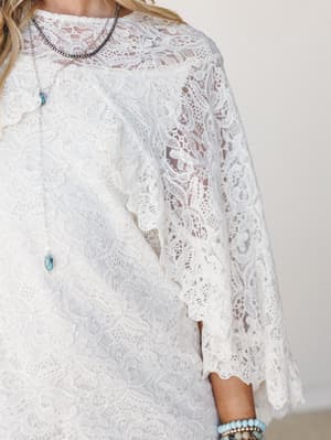 A close-up of an ivory lace dress with wide bell sleeves and scalloped edges, styled with layered turquoise and silver jewelry for a romantic, boho-southwestern feel.