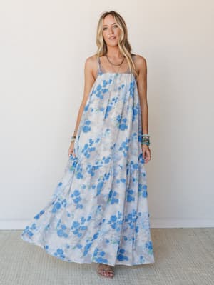 A flowy floral maxi dress in soft white and blue roses styled with layered bracelets and a delicate necklace — the kind of dress that moves when you walk and makes every errand feel a little more like a summer afternoon.