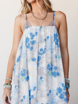 A flowy floral maxi dress in a soft watercolor blue rose print, styled with layered turquoise necklaces and stacked beaded bracelets — the kind of dress that feels like a daydream you actually got dressed in.