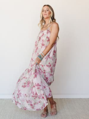 A flowy floral maxi dress in soft blush and mauve rose tones styled with stacked turquoise bracelets and slide sandals — the kind of dress that looks equally at home at a garden party or a slow Saturday morning.