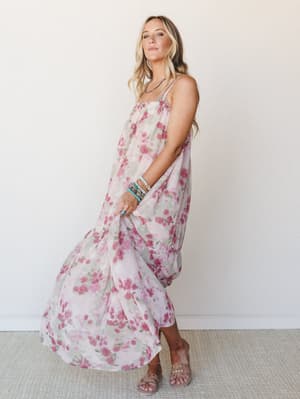 A flowy floral maxi dress in soft blush and mauve rose tones styled with stacked turquoise bracelets and slide sandals — the kind of dress that looks equally at home at a garden party or a slow Saturday morning.