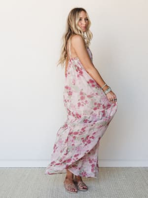 A flowy floral maxi dress in soft mauve and rose catches mid-twirl against a clean white wall — the kind of dress that makes you want to spin just to see what it does.