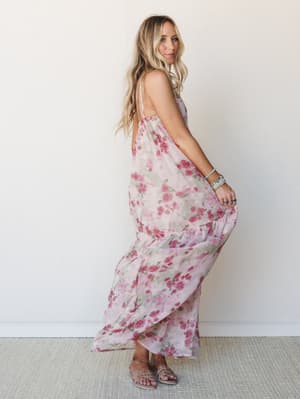 A flowy floral maxi dress in soft mauve and rose catches mid-twirl against a clean white wall — the kind of dress that makes you want to spin just to see what it does.