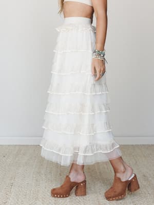 A dreamy ivory tiered ruffle maxi skirt styled with a cropped top and brown suede studded clogs — the kind of outfit that makes a bridal shower feel effortless and a festival feel fancy.