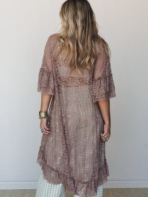 Shot from behind, a model layers a sheer taupe lace duster kimono over gingham wide-leg pants, styled with stacked boho jewelry — the kind of outfit that looks like it came together effortlessly but definitely didn't.