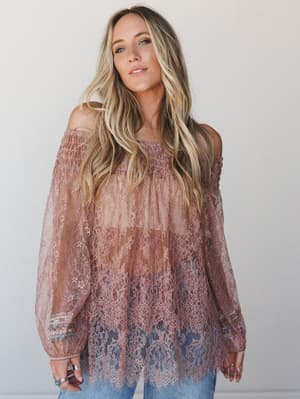 A flowy off-shoulder lace tunic in dusty mauve-brown worn over light wash denim, with romantic scalloped hem details and smocked neckline — the kind of top that looks equally at home at a winery or a Saturday farmers market.
