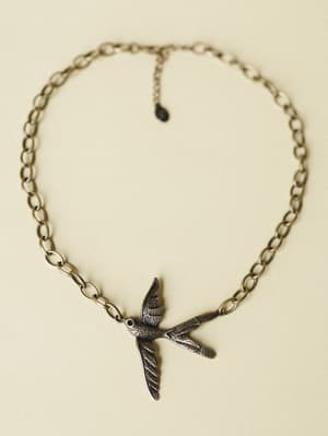 A chunky bronze chain necklace laid flat, centered by a detailed oxidized bird pendant mid-flight — the kind of piece that feels like it has a story before you even put it on.