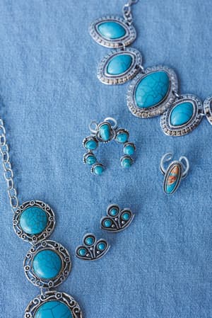 The Celia Blossom Turquoise Ring, featuring ornate silver detailing and a vibrant turquoise stone with natural veining, is displayed on a blue fabric background.
