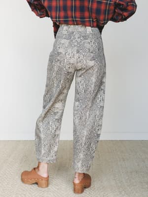 Shot from behind, these barrel-leg snakeskin print jeans are styled with a plaid flannel and wooden clogs — an earthy, lived-in mix that feels effortlessly cool without trying too hard.