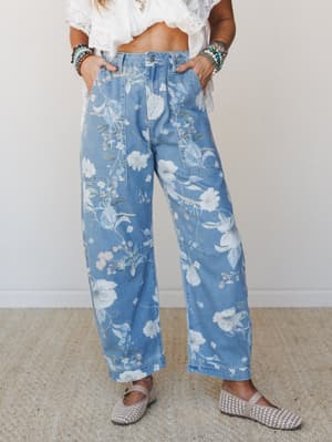 Wide-leg floral denim jeans in a soft medium wash, styled with a cropped white lace top, woven flats, and stacked beaded bracelets — the kind of outfit that makes a farmers market feel like an event.