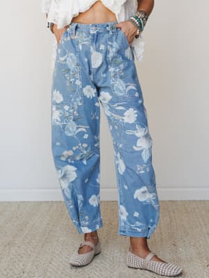 Wide-leg floral denim jeans in a soft medium wash, styled with a white lace crop top, woven flats, and stacked beaded bracelets — the kind of outfit that looks effortless but was absolutely thought about.