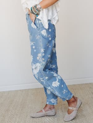A side-profile shot of floral-printed medium wash denim barrel jeans styled with a white lace-hem top, stacked turquoise bracelets, and woven Mary Jane flats — the kind of outfit that looks effortless but was absolutely thought about.