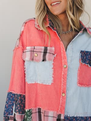 A close-up of a patchwork button-down shacket layering coral corduroy, pale blue corduroy, navy floral cotton, and pink plaid — all stitched together with raw frayed edges for a lived-in, collected feel.