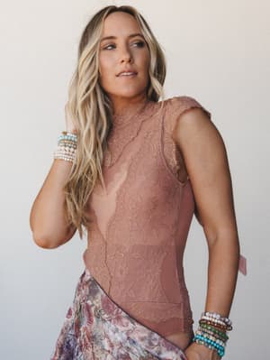 A dreamy close-up of a model in a terracotta lace bodysuit layered over a floral skirt, both wrists stacked with beaded bracelets — the kind of outfit that feels effortless and intentional at the same time.