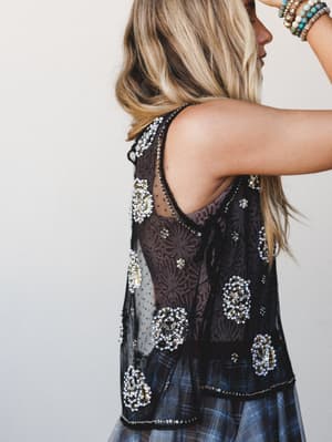 A close back-angle shot of a beaded black mesh tank layered over a plaid skirt — the kind of top that makes a simple outfit feel like it has a secret, styled with stacked boho bracelets for that effortlessly collected look.