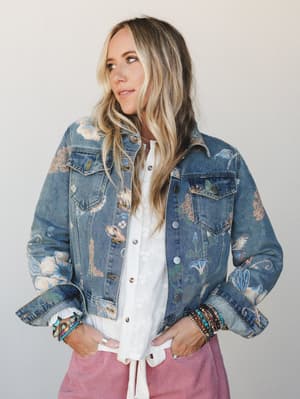 A floral-printed denim jacket layered over a white tie-front top and dusty pink corduroy pants, styled with stacked boho bracelets — the kind of outfit that looks effortless but clearly had a moment of intention behind it.