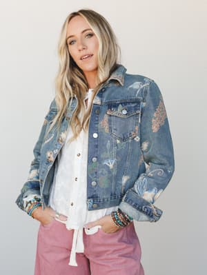 A floral-printed denim jacket layered over a white tie-front top and dusty pink corduroy pants, styled with stacked beaded bracelets — the kind of outfit that looks like it came together effortlessly but definitely didn't.