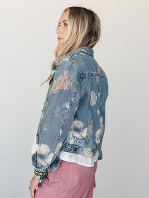A side-profile shot of a floral-printed denim jacket layered over a white top and dusty pink corduroy pants — the kind of piece that looks like it wandered out of a garden and never looked back.