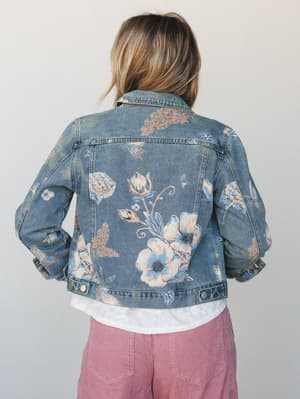 A floral-printed denim jacket shot from the back, layered over a white top and dusty rose corduroy pants — the kind of piece that makes a regular Tuesday feel a little more intentional.