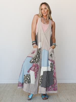 A wide-leg patchwork jumpsuit in light taupe layered over a blush pink tank, styled with stacked beaded bracelets, a layered silver necklace, and turquoise sandals — the kind of outfit that looks like it has a whole story behind it.