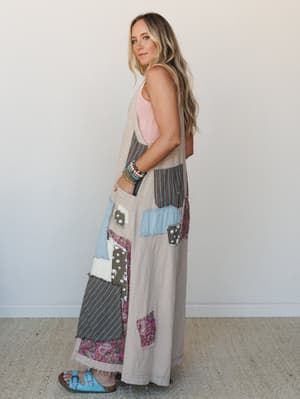 A breezy side-profile shot of a wide-leg patchwork jumpsuit in light taupe, layered with a blush pink knit tank and styled with turquoise sandals and beaded bracelets — the kind of outfit that looks like it was collected, not coordinated.