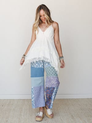 A flowy white lace-trim cami top paired with wide-leg patchwork pants in mixed blue prints — daisy, paisley, bandana, and denim — styled with platform espadrille sandals and stacked bracelets for a free-spirited, collected look.